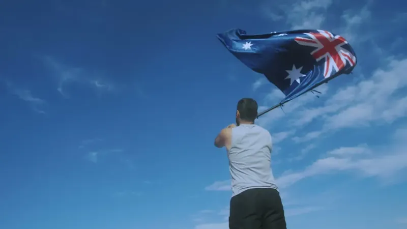 A man waving the Australian flag against a blue sky